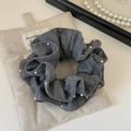 Dettaglio di un elastico per capelli in maglia grigia con perle su un sacchetto in tessuto - Grigio