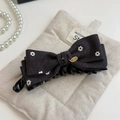 Detail van gebloemde denim haarklem met gouden metalen plaat op beige linnen stof - Zwart en Grijs