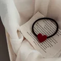 Close-up of red heart charm on elastic black hair tie against vintage fabric background - Red