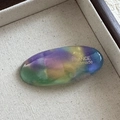 Close-up of handmade oval acetate hair clip featuring colorful gradient and gold logo - Macarons