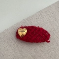 Detailed macro view of red tweed fabric hair clip with a gold heart hammer emblem - Heart Label