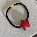 Dettaglio di elastico per capelli con stella rossa glitterata e chiusura in metallo oro - Pentagramma