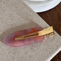 Détail d'une pince à cheveux en résine marbrée avec base en métal doré sur lin - Rose Pourpre