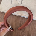Detail of caramel brown padded satin headband featuring a black woven brand label on wood - Brown