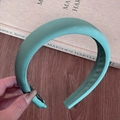 Detail of mint green padded satin headband showing lustrous fabric texture on a desk - Cyan