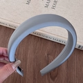 Detail view of thick grey padded headband with satin texture held against a wooden desk - Gray