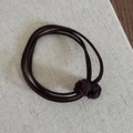 Dettaglio di un elastico per capelli intrecciato marrone con due nodi decorativi - Caffè Scuro