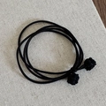 Dettaglio di un elastico per capelli nero con nodi intrecciati a mano su tela beige chiaro - Nero