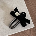 Detail view of black velvet bow hair clip with sparkling rhinestones and metal label - Black
