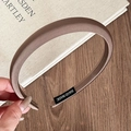 Detail eines kaffeebraunen Satin-Stirnbandes mit Handmade-Etikett auf Holzhintergrund - Braun