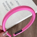 Detailed macro view of magenta satin padded headband with handmade label on top of books - Rose Red