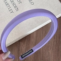 Detailed shot of purple satin fabric headband with white handmade label on interior edge - Purple