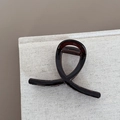 Detail view of the brown resin hair claw clip with crossed loop design on linen texture - X Shape Style / Transparent Tea