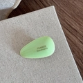 Makroaufnahme einer hellgrünen Acetat-Haarspange in Tropfenform mit goldenem Logo - Grün
