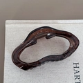 Detailed macro view of the wave-shaped amber brown hair claw clip with its metal spring - Irregular Style / Transparent Tea