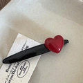 Detailopname van een rode hartvormige haarclip met een zwarte eendenbekbasis op een blad - Zwart