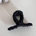 Dettaglio della molletta per capelli in tessuto nero satinato su superficie in pelle crema - Forma X Nera