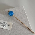 Detail van een gouden haarspeld met blauw gemarmerde bol op getextureerde stof - Blauw