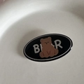 Detail of a black oval drip glue hair clip featuring a cute brown cartoon bear and BEAR text - Black Bear