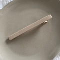 Dettaglio di un fermaglio a becco d'anatra minimalista in tessuto beige su vassoio ceramico - Bianco Sporco