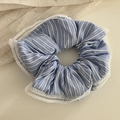 Dettaglio di uno scrunchie a righe blu con pizzo bianco su sfondo di tessuto naturale - Stile con Bordo in Pizzo / Elastico Pizzo A Righe Blu