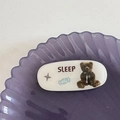 Détail d'une pince à cheveux ovale blanche en résine avec motif ours et texte SLEEP - Ours Blanc