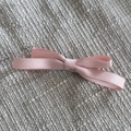 Detail view of a pink ribbon bow hair clip with satin texture on a grey woven surface - Pink