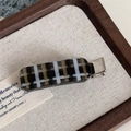 Detailed macro view of a brown plaid acetate hair clip on a metal alligator base - Black Check