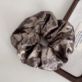 Dettaglio dell'elastico in raso bronzo con eleganti motivi floreali neri e finitura lucida - Elastico per capelli marrone