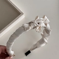 Dettaglio di un cerchietto elegante in raso plissettato con fiocco color oro champagne - Beige