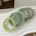 Close-up of green spiral phone cord hair ties set with heart patterns on ceramic tray - Green Series