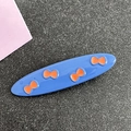 Detail shot of a blue oval hair clip featuring orange bow prints and polished metal finish - Oval / Blue