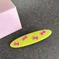Detail of green oval hair clip with pink bow prints on a textured background - Oval / Yellow-Green