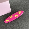 Rose pink oval hair clip with yellow bow patterns for girls, shown on a textured surface - Oval / Rose Pink