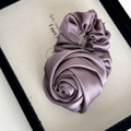 Nahaufnahme eines eleganten Satin-Haargummis in Rosenform, Morandi-Lila Seidentextur - Bohnenpastenviolett