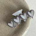 Detalle de pinza de pelo gris con forma de corazón y acabado mate en un plato sencillo - Corazón Gris Con Borde Blanco