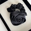 Detailaufnahme des eleganten schwarzen Satin-Rosen-Haargummis mit feiner Stoffstruktur - Schwarz