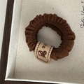 Détail d'un chouchou en tricot marron foncé avec étiquette ours et texte Cake - Café foncé