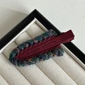 Macro view of burgundy knitted hair clip with multi-color woven edges on a velvet tray - Red