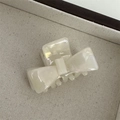 Detail of a pearl white marble texture bow hair claw clip on a beige fabric tray - White