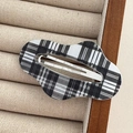 Macro detail of wave-shaped black and white plaid hair clip on a beige velvet tray - Cloud-Black Plaid