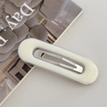 Detalle de una pinza ovalada de resina blanca con diseño de estructura metálica plateada - Blanco