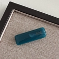 Detailed view of glossy dark teal French barrette with gold lettering on grey texture - Green