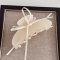 Detail shot of a cream white bow claw clip with glossy finish and ribbon on a soft tray - Milk White