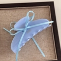 Detail view of a light blue bow hair claw clip with ribbon on a textured tray - Blue