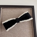 Close-up of elegant black fabric bow hair clip with white pearl bead edging on a tray - White