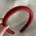 Detail of dark red textured wool headband with a handmade label on beige linen background - Red