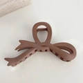Primer plano de pinza de pelo con lazo marrón mate y textura esmerilada en fondo beige liso - Café claro