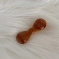 Close-up of amber acetate bow hair clip with gold logo on a white faux fur background - Light Coffee