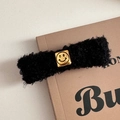 Nahaufnahme einer schwarzen lockigen Lammfell-Haarklammer mit goldener quadratischer Smileyschnalle - Smiley Schwarzer Clip